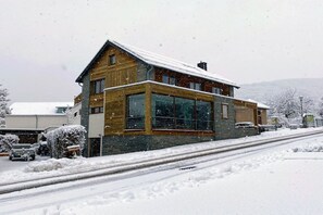 Een houten huis met twee verdiepingen, grote ramen en een sneeuwbedekte kap.