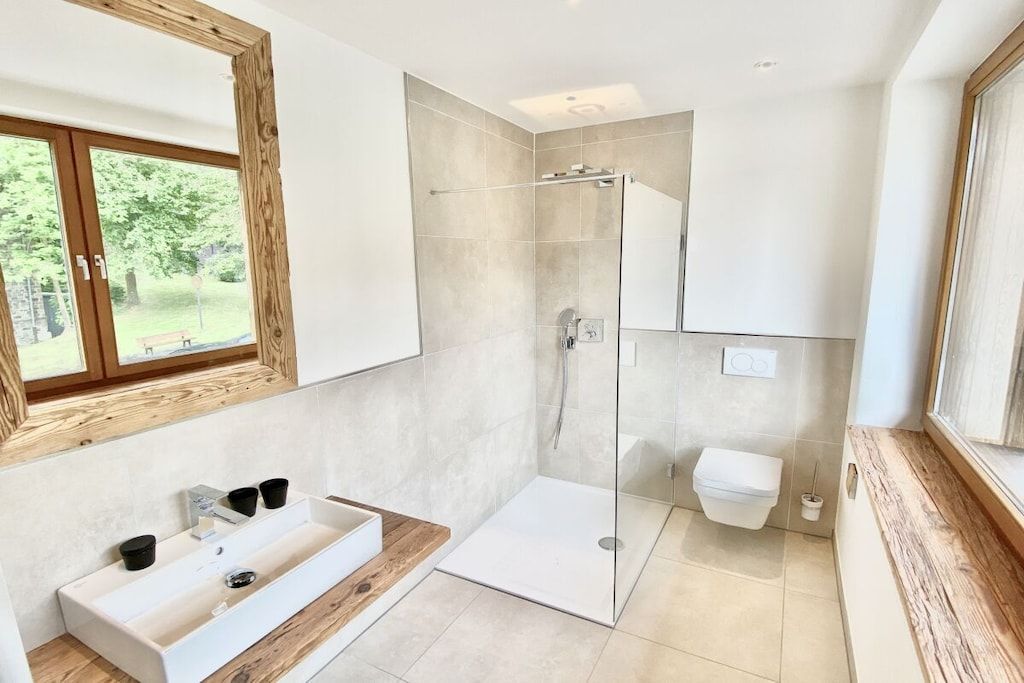 A modern bathroom with a glass shower enclosure, a white sink with a wooden countertop, and a large mirror above the sink.