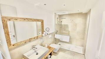 A modern bathroom with a wooden vanity, a large mirror, a bathtub, and a glass-enclosed shower.