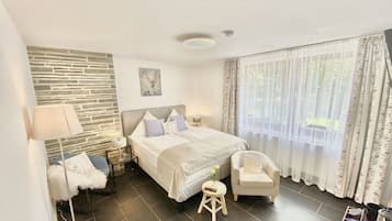 A modern hotel room with a stone accent wall, a large bed with pillows, a bedside table, a chair, and a window with curtains.