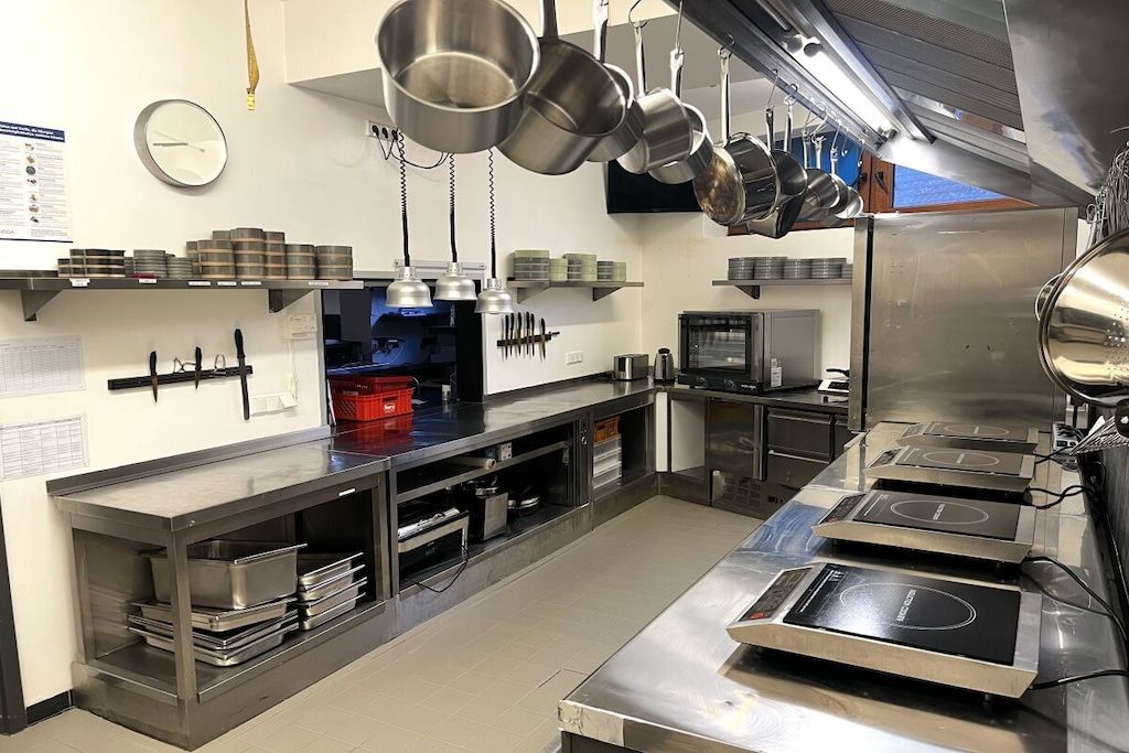 Une cuisine professionnelle équipée d’appareils en acier inoxydable, de casseroles suspendues et d’une horloge au mur.