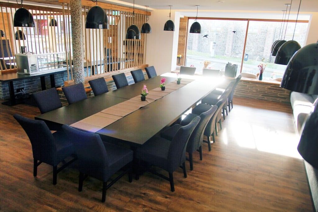 Un espace de salle à manger moderne, avec une longue table, des chaises, des luminaires suspendus et une vue dégagée grâce à de grandes fenêtres.