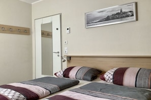 Ein Hotelzimmer mit einem Bett, einer Tür, einem Kleiderhaken, einem an der Wand befestigten Lichtschalter und einem gerahmten Bild.