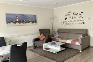 Ein modernes Wohnzimmer mit einer Couch, einem Sessel, einem Couchtisch und einem Gemälde von einem Leuchtturm.