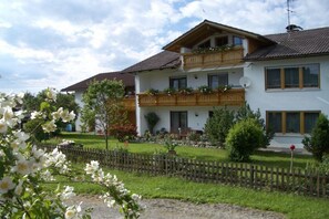 A two-story house with a balcony, surrounded by a wooden fence and a garden. - Holiday apartment with 2 bedrooms (Roßhaupten)
