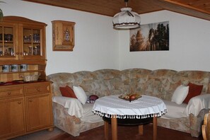 Un salon avec un canapé à motifs, un meuble en bois et une table sur laquelle se trouve un panier de fruits.