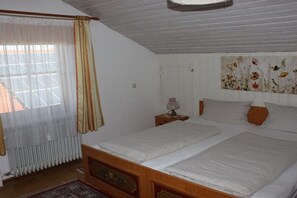 A bedroom with two beds, a radiator, a nightstand with a lamp, and a floral wall decoration. - Holiday apartment with 2 bedrooms (Roßhaupten)