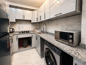 A modern kitchen with white cabinets, a built-in oven, a microwave, and a washing machine. - 3BRs AlAlson Institute Nasr City Fancy Apart (Cairo Governorate)