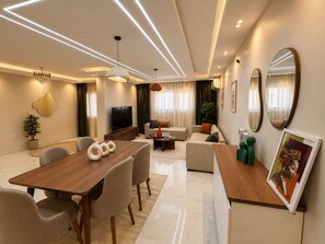 A modern living room with a dining area, a television, and a painting. - 3BRs AlAlson Institute Nasr City Fancy Apart (Cairo Governorate)