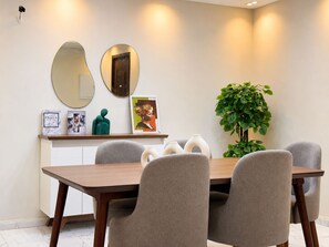 A dining area with a wooden table, grey upholstered chairs, a potted plant, and wall-mounted artwork. - 3BRs AlAlson Institute Nasr City Fancy Apart (Cairo Governorate)