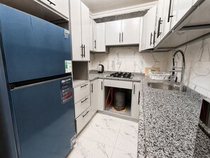 A kitchen with white cabinets, a blue refrigerator, a gas stove, and a sink. - 3BRs AlAlson Institute Nasr City Fancy Apart (Cairo Governorate)