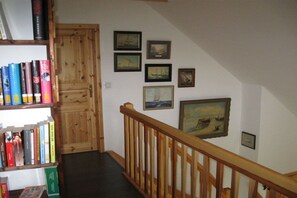 A staircase with a wooden handrail leading to a landing with a bookshelf and framed pictures on the wall. - Holiday home with 2 bedrooms (Greetsiel)