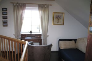 A room with a wooden crib, a desk with a lamp, a sofa, and a framed picture on the wall. - Holiday home with 2 bedrooms (Greetsiel)