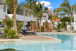 A pool area with lounge chairs and palm trees. - The Bank | Luxe Penthouses | 5 min Mambo&Jan thiel (Willemstad)