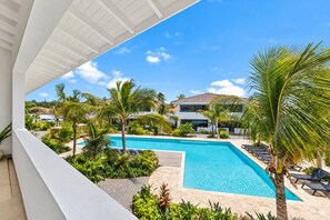 Ein Poolbereich mit Liegestühlen und Palmen, ein klarer, blauer Himmel und ein Gebäude im Hintergrund.