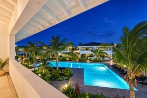 A swimming pool with surrounding palm trees and a modern building in the background. - The Bank | Luxe Penthouses | 5 min Mambo&Jan thiel (Willemstad)