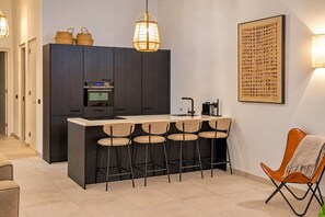 Cuina moderna amb una illa central, tamborets i il·luminació penjant.