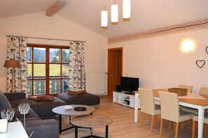 A modern living room with a sofa, a coffee table, a dining area with chairs, a television, and a window with curtains. - Holiday apartment with 2 bedrooms (Bodenmais)