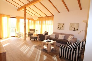 Ein geräumiges Wohnzimmer mit Holzboden, einer Sofagarnitur, einem Couchtisch und einer Stehlampe.