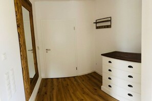 A room with a white door, wooden flooring, and a white dresser with multiple drawers. - Holiday apartment with a view of the sluice (Neuharlingersiel)