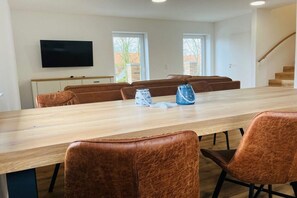 A dining area with a long table, brown upholstered chairs, and a television mounted on the wall. - Holiday apartment with a view of the sluice (Neuharlingersiel)