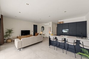 Una sala moderna con un sofá, televisor y un comedor con taburetes de bar.