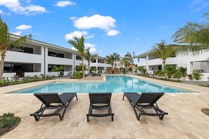 A swimming pool with lounge chairs, surrounded by modern buildings and palm trees. - The Bank | Poolside Apt. | 5m to Mambo & Jan Thiel (Willemstad)