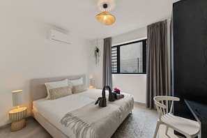 A modern bedroom with a large bed, bedside lamps, a desk, and a view of the outdoors. - The Bank | Poolside Apt. | 5m to Mambo & Jan Thiel (Willemstad)