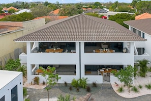 A multi-story residential building with a tiled roof, outdoor seating areas, and a landscaped garden. - The Bank | Poolside Apt. | 5m to Mambo & Jan Thiel (Willemstad)