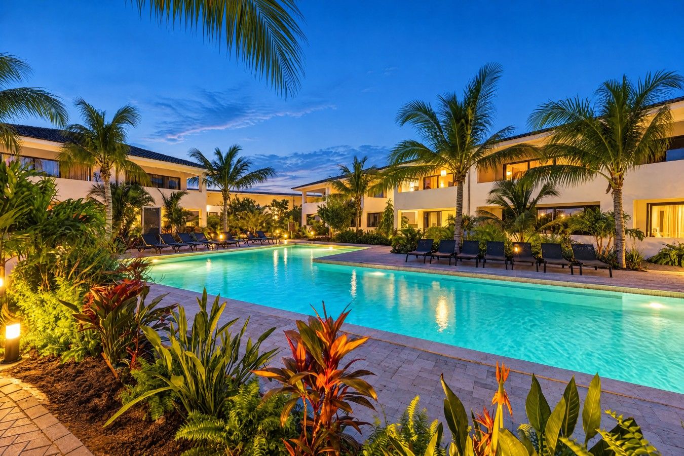 Una piscina con sillones de descanso, palmeras y un edificio con varios balcones.
