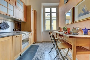 A kitchen with wooden cabinets, a stove, and a window with a view of buildings. - Vatican City View | 2 Bedrooms & 2 Bathrooms (ROMA)