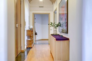 Een hal met een houten vloer, een receptiebalie met een bloemenvaas en een lijst met een afbeelding aan de muur.