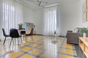A modern living room with a checkered floor, a dining area with chairs and a table, a sofa, and a painting on the wall. - Vatican City View | 2 Bedrooms & 2 Bathrooms (ROMA)