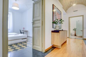 A hotel room with a bed, a bedside table, a chair, a small table, a potted plant, and a bathroom visible through an open door. - Vatican City View | 2 Bedrooms & 2 Bathrooms (ROMA)