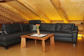 A modern loft-style room with a black leather sectional sofa, a wooden coffee table, and a wooden ceiling with exposed beams. - Canadian Luxury Chalet (Leisel)