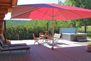 A wooden deck with outdoor furniture, a hot tub, and a large umbrella providing shade. - Canadian Luxury Chalet (Leisel)