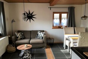 A cozy living room with a sofa, a small round table, and a window with curtains. - Holiday home in Allgäu with 2 bedrooms (Sonthofen)