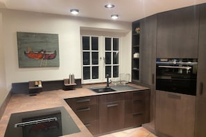 A modern kitchen with a built-in oven, a sink, and a window with white frames. - Landhaus Wattwiesen (Mediterranean) (Rantum)