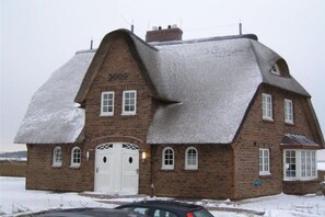 A brick building with a steeply pitched roof, a white door, and multiple windows. - Landhaus Wattwiesen (Mediterranean) (Rantum)