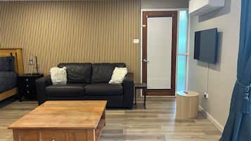 A modern living room with a wooden coffee table, black leather sofa, and a TV mounted on the wall.