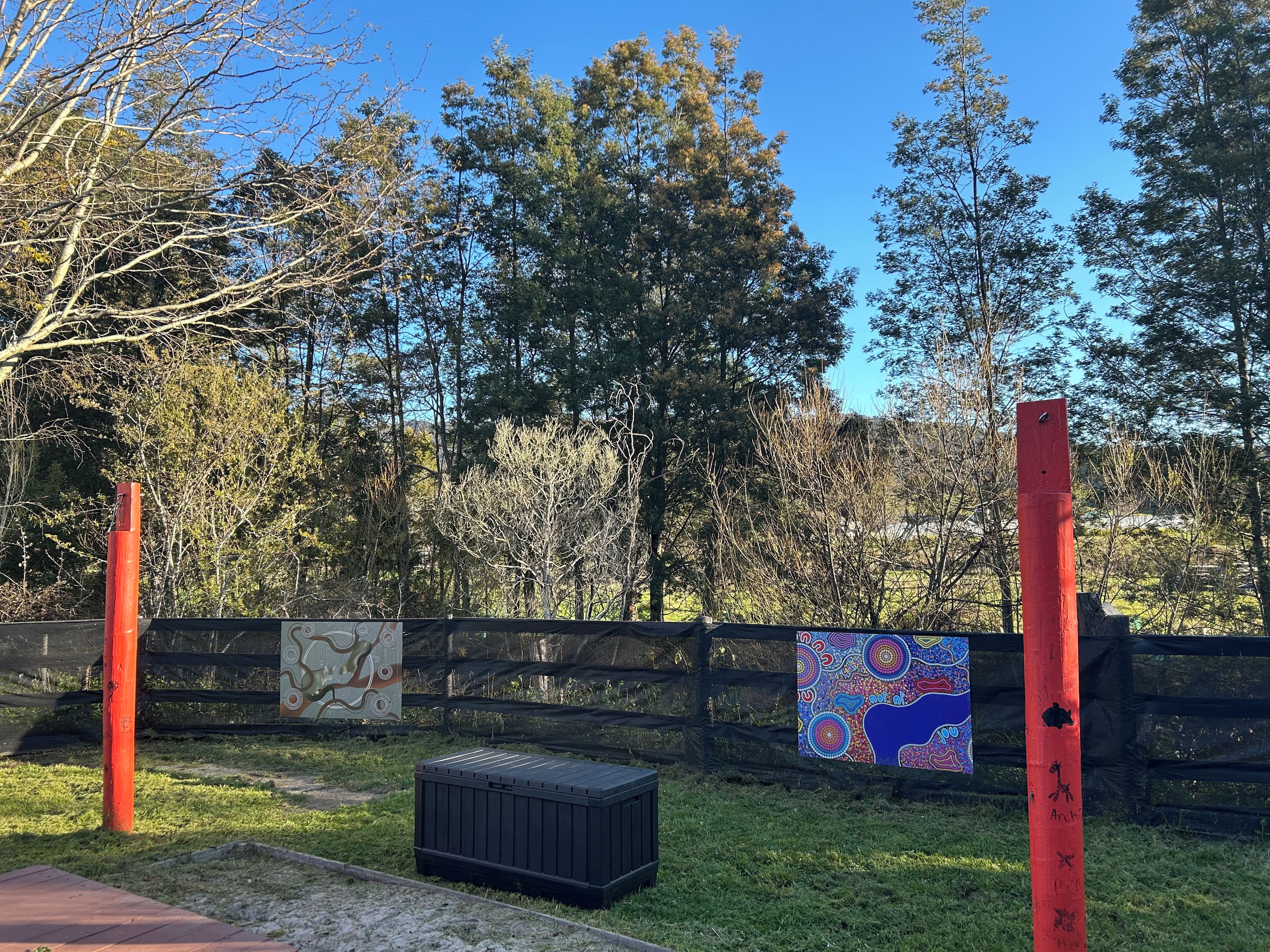 Un espacio exterior cercado con una caja de almacenamiento negra, un mural colorido y un cielo azul despejado.