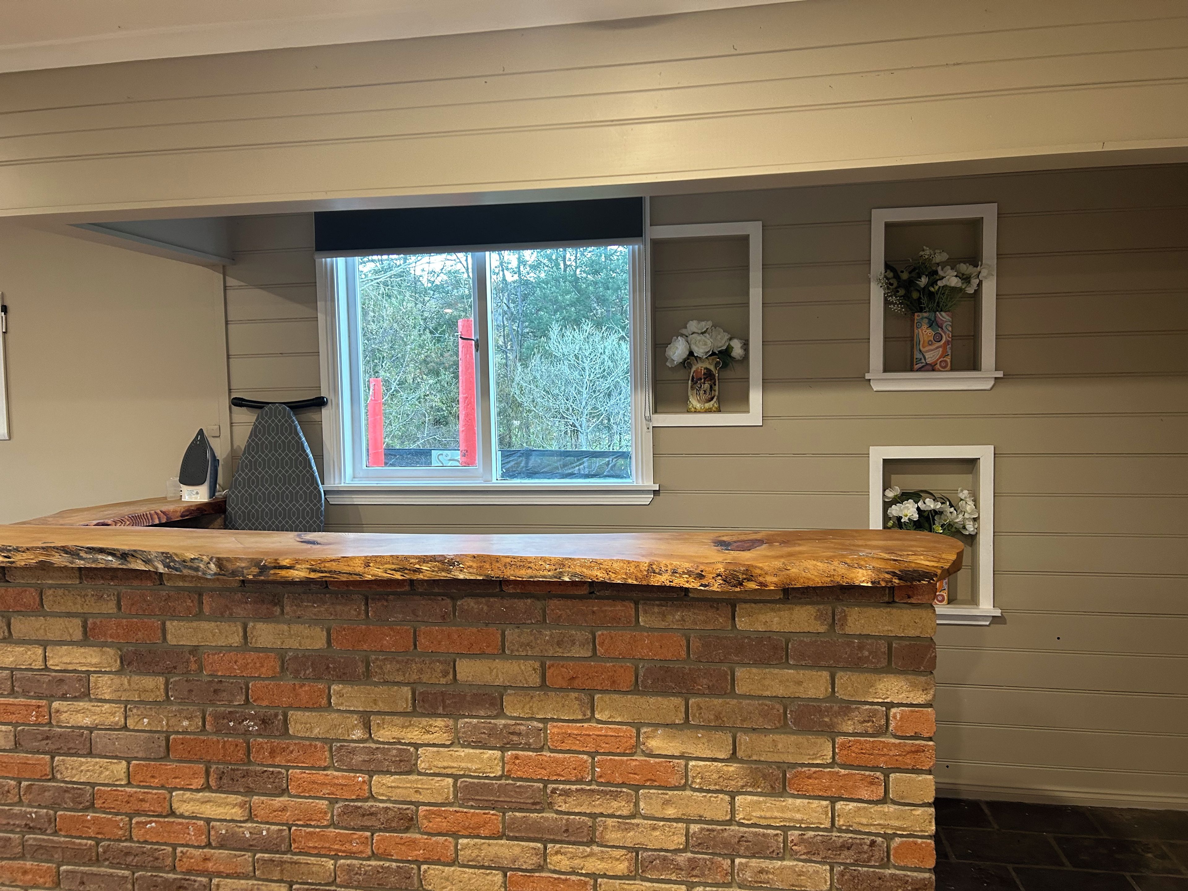 A kitchen with a brick counter, a window with a view of trees, and decorative shelves with flowers.