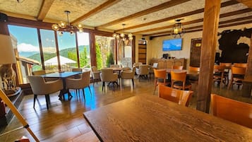 A dining area with multiple tables and chairs, a television mounted on the wall, and a view of the outdoors.