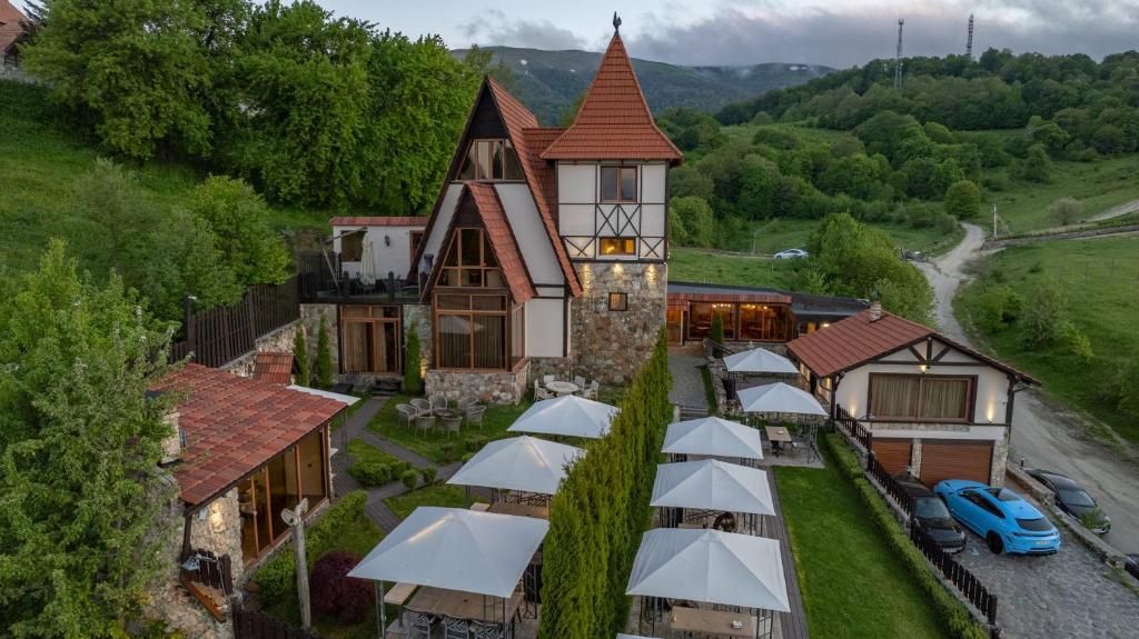 A traditional chalet-style hotel with a prominent tower, multiple dining areas with umbrellas, and a scenic mountainous backdrop.