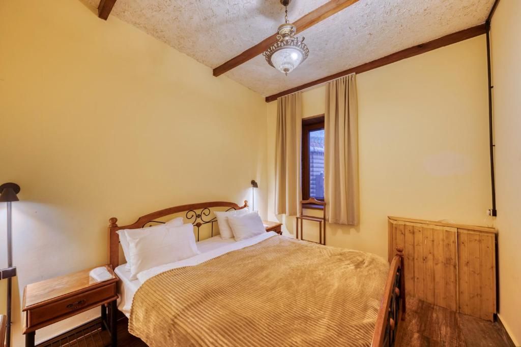 A bedroom with a wooden bed, a nightstand, a lamp, a window with curtains, and a wooden radiator.