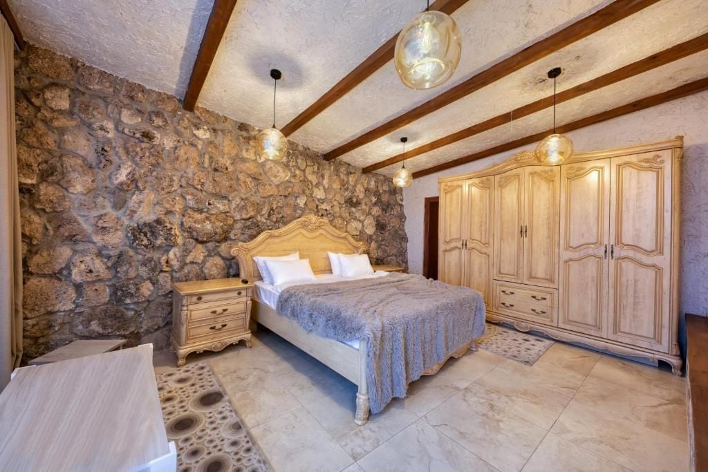 A bedroom with a stone wall, wooden bed frame, and a large wardrobe.