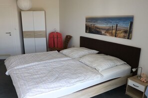 Ein Schlafzimmer mit Bett, Kleiderschrank, Nachttisch und Wandbild mit Strandmotiv.