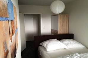 Ein Schlafzimmer mit einem Bett, einer Tür, einem Spiegel und einer Pendelleuchte.