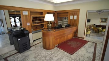 A hotel reception area with a wooden desk, a lamp, a printer, and a red carpet.