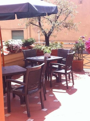 An outdoor patio with tables and chairs, a tree, and potted plants. - Hotel Grande Bretagne (Montecatini Terme)